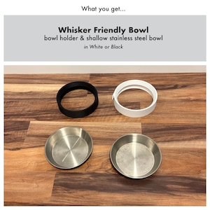 Op de afbeelding: Een huisdierenset met een zwarte en een witte komhouder en twee ondiepe roestvrijstalen kommen. De tekst luidt "Whisker Friendly Bowl" en "bowl holder & shallow stainless steel bowl in White or Black."