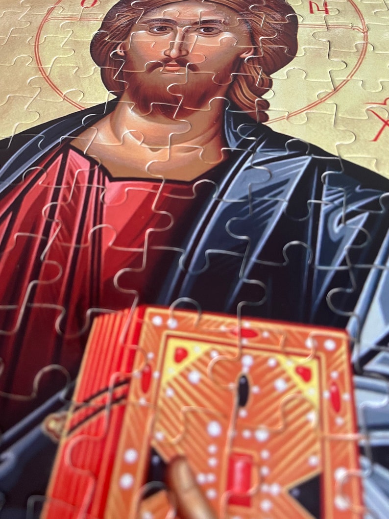 May include: A jigsaw puzzle depicting a religious icon of Jesus Christ holding a book. The icon is painted in a traditional style with a red and blue robe and a gold halo. The puzzle pieces are visible in the image.