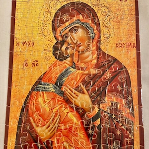 May include: A jigsaw puzzle depicting a religious icon of the Virgin Mary holding baby Jesus. The icon is painted in a traditional style with gold and red colors. The puzzle is made of wood and has a finished size of 10 inches by 8 inches.