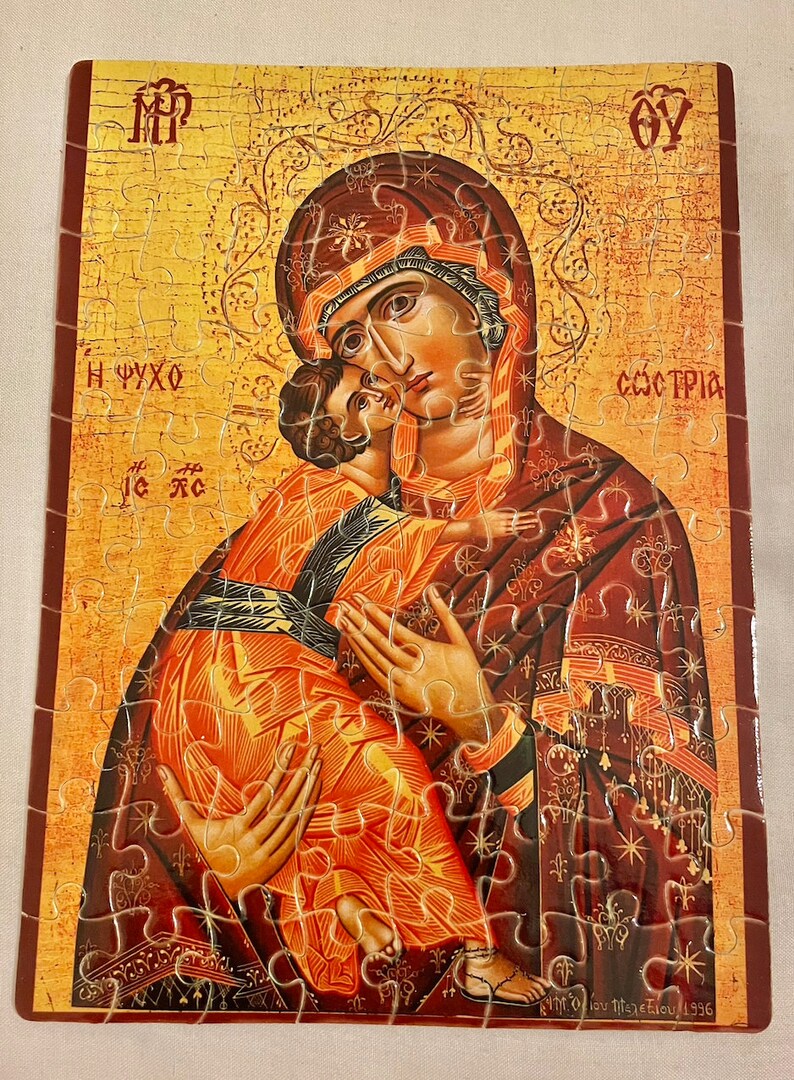 May include: A jigsaw puzzle depicting a religious icon of the Virgin Mary holding baby Jesus. The icon is painted in a traditional style with gold and red colors. The puzzle is made of wood and has a finished size of 10 inches by 8 inches.