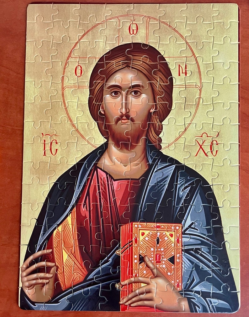May include: A religious icon puzzle featuring a depiction of Jesus Christ holding a book. The icon is painted in a traditional style with gold accents and the text "IC XC" in red.