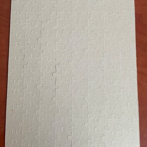 May include: A blank white jigsaw puzzle with a textured surface. The puzzle is made of cardboard and has a standard interlocking design.