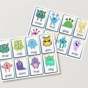 May include: Two sets of flashcards featuring colorful cartoon monsters. Each card has a unique monster illustration and a corresponding word. The cards are white with a blue border and are arranged on a light background.