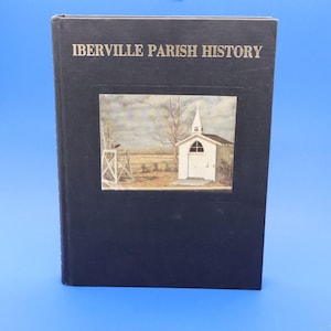 May include: A hardcover book titled "IBERVILLE PARISH HISTORY" with a black cover. The cover features a framed painting of a white church with a steeple, set against a rural landscape with a windmill.