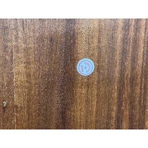 May include: Close-up of a wooden surface with a visible wood grain pattern. A small, round sticker with the text "MADE IN PHILIPPINES" in a blue and pink color scheme is affixed to the wood.