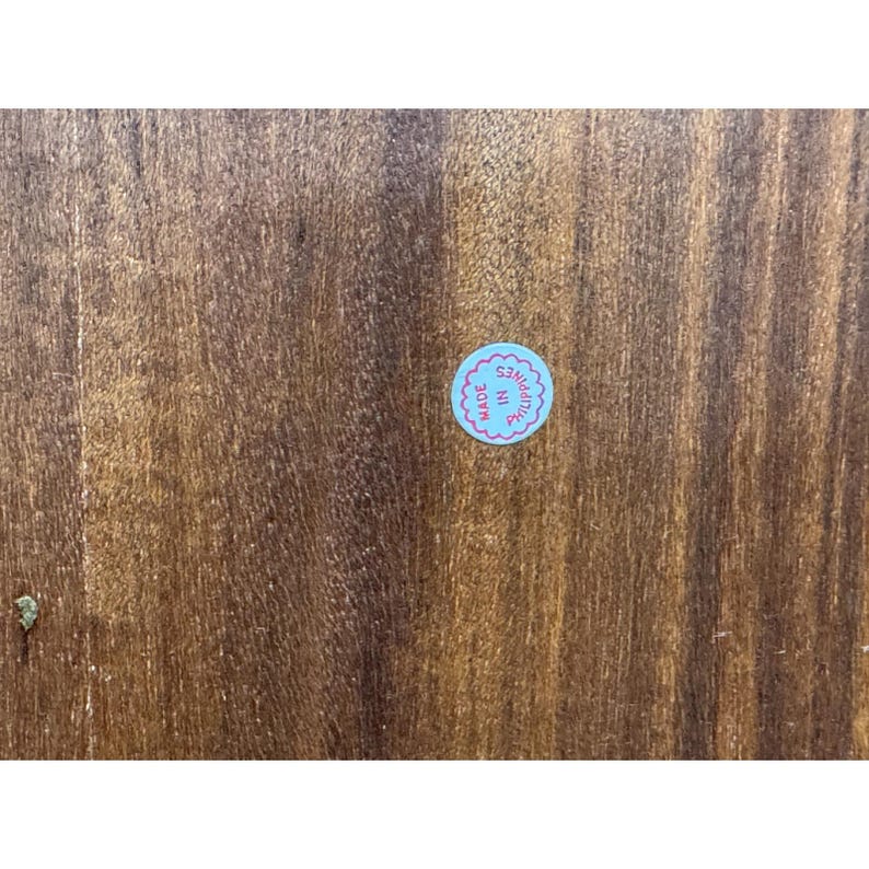 May include: Close-up of a wooden surface with a visible wood grain pattern. A small, round sticker with the text "MADE IN PHILIPPINES" in a blue and pink color scheme is affixed to the wood.