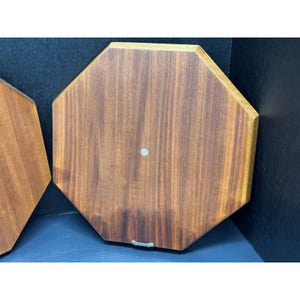 May include: Two octagonal wooden plaques with a warm brown finish. Each plaque has a small, light-colored dot in the center and a metal hanger on the bottom edge. The wood grain is visible.