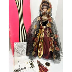 May include: A collectible doll in a burgundy and gold gown, adorned with autumn-themed leaf accents and a black mesh cape. The doll is displayed with its original packaging and certificates.