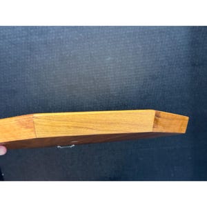 May include: A wooden, octagonal-shaped tray with a light brown finish. The tray has a flat surface and angled sides. The wood grain is visible. The tray is held by a hand, with a dark background.