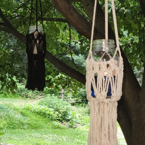May include: Two macrame hanging candle holders with glass jars. One is black and the other is white with a blue glass jar.