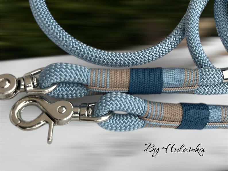 May include: Close-up of a light blue dog leash with silver metal clasps. The leash features a woven rope design with sections of blue, tan, and navy blue. The text "By Hulamka" is visible in the bottom right corner.