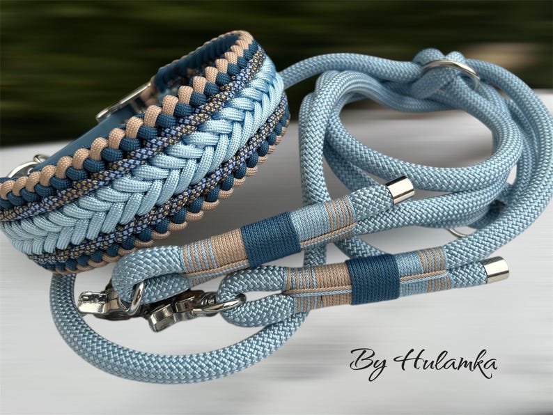May include: A dog collar and leash set in shades of blue and tan. The collar features a braided design with a silver buckle. The leash and collar are made of a sturdy rope material. The text "By Hulamka" is visible.