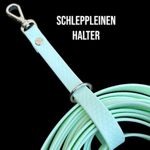 Può includere: Un guinzaglio per cani di colore verde chiaro con un moschettone argentato e un motivo esagonale. Il guinzaglio è arrotolato e il testo "SCHLEPPLEINEN HALTER" è visibile.