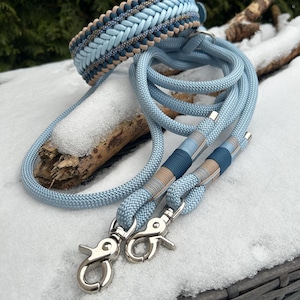 May include: A light blue dog collar and matching leash set. The collar features a braided design with light blue, tan, and navy blue accents. The leash has a light blue rope with silver-colored clasps.
