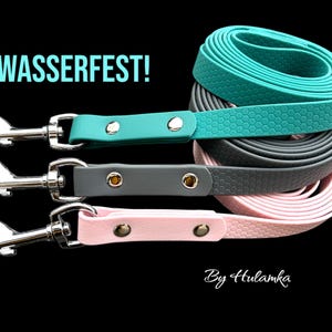 Puede incluir: Tres correas para perros en color turquesa, gris y rosa con cierres metálicos a juego. Las correas están hechas de un material texturizado e impermeable. El texto "WASSERFEST!" es visible en la imagen. El texto "By Hulamka" también es visible en la imagen.