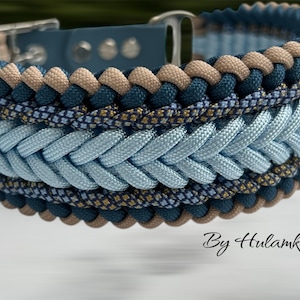 May include: A braided dog collar in shades of blue, tan, and navy. The collar features a light blue braided center, bordered by navy and tan rope. The collar has a silver-colored buckle and is labeled "By Hulamka".