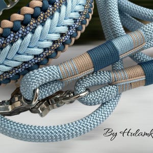 May include: Close-up of a dog collar and leash set in shades of blue and tan. The collar and leash are made of braided rope with metal hardware. The leash handle and collar feature decorative accents. The text "By Hulamka" is visible.