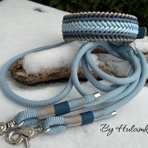May include: A braided dog collar and matching leash set in shades of blue and tan. The collar features a woven design, and the leash has silver-tone metal clasps. The set is displayed on a snowy surface.