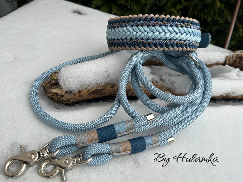 May include: A braided dog collar and matching leash set in shades of blue and tan. The collar features a woven design, and the leash has silver-tone metal clasps. The set is displayed on a snowy surface.