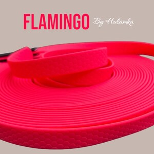 Può includere: Un guinzaglio per cani arrotolato di colore rosa acceso con un manico nero. Il guinzaglio è etichettato "FLAMINGO By Hulamka".