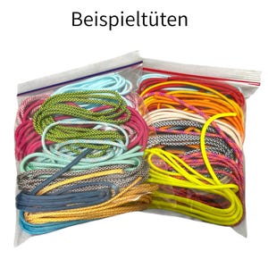 Könnte beinhalten: Zwei transparente Plastiktüten gefüllt mit bunten Schnürsenkeln. Die Schnürsenkel sind in verschiedenen Farben erhältlich, darunter Blau, Rosa, Grün, Gelb und Gold. Der Text "Beispieltueten" ist oben aufgedruckt.