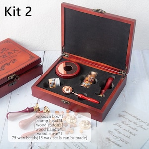 May include: A wax seal kit in a dark wood box labeled Kit 2, containing a metal melting spoon with a red handle, a red wax seal stamp, two glass jars of wax beads, and a wood stove. Text lists: wooden box*1, stamp head*1, wood spoon*1, wood handle*1, wood stove*1, 75 wax beads.