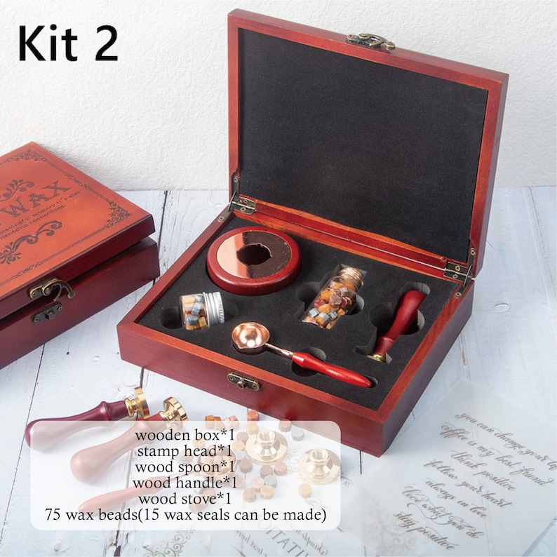 May include: A wax seal kit in a dark wood box labeled Kit 2, containing a metal melting spoon with a red handle, a red wax seal stamp, two glass jars of wax beads, and a wood stove. Text lists: wooden box*1, stamp head*1, wood spoon*1, wood handle*1, wood stove*1, 75 wax beads.