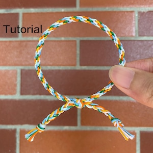 May include: A tutorial for making a friendship bracelet with blue, white, orange and green threads. The bracelet is tied in a knot at the end.