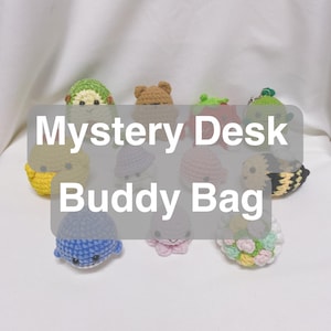 Puede incluir: Una colección de pequeños amigos de escritorio de ganchillo en varios colores y diseños. El texto "Mystery Desk Buddy Bag" está superpuesto en la imagen. Los amigos incluyen un oso, una ballena, una abeja y otras criaturas.