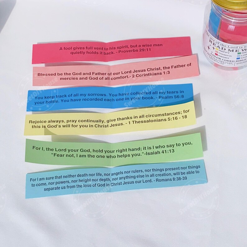 Op de afbeelding: Een glazen pot gevuld met kleurrijke papieren stroken met inspirerende Bijbelteksten. De pot heeft een gouden deksel en een label met de tekst "Read Me Words of the Lord".
