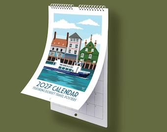 May include: A 2027 wall calendar featuring Dorset travel posters with a spiral binding. The cover displays a colorful illustration of a boat on water in front of buildings, with the text 2027 CALENDAR FEATURING DORSET TRAVEL POSTERS printed below.