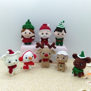 Könnte beinhalten: Eine Sammlung von acht gehäkelten Weihnachtsornamenten, darunter der Weihnachtsmann, ein Rentier, ein Schneemann, ein Lebkuchenmann, ein Elf und ein Bär. Die Ornamente sind alle handgefertigt und weisen leuchtende Farben und festliche Details auf.