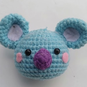 May include: A blue crocheted koala plush toy with purple nose, pink cheeks, and black eyes.