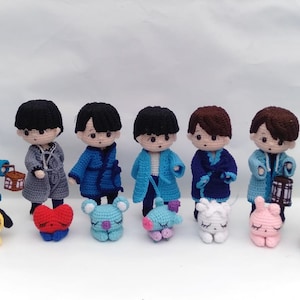 Könnte beinhalten: Eine Sammlung handgefertigter Häkelpuppen, die jeweils eine Figur in verschiedenen Outfits mit schwarzen oder braunen Haaren darstellen. Begleitet werden die Puppen von kleineren Häkelfiguren von Tieren und Laternen. Die Puppen sind etwa 13 cm groß.