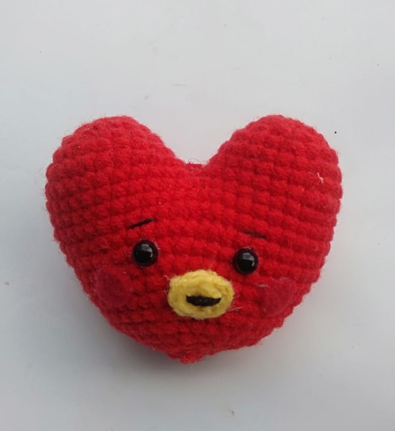 May include: Red crocheted heart-shaped plush toy with a yellow nose, black eyes, and a smiling expression.