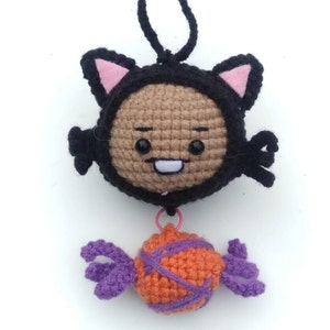 May include: Crocheted black cat with pink ears holding an orange and purple candy.