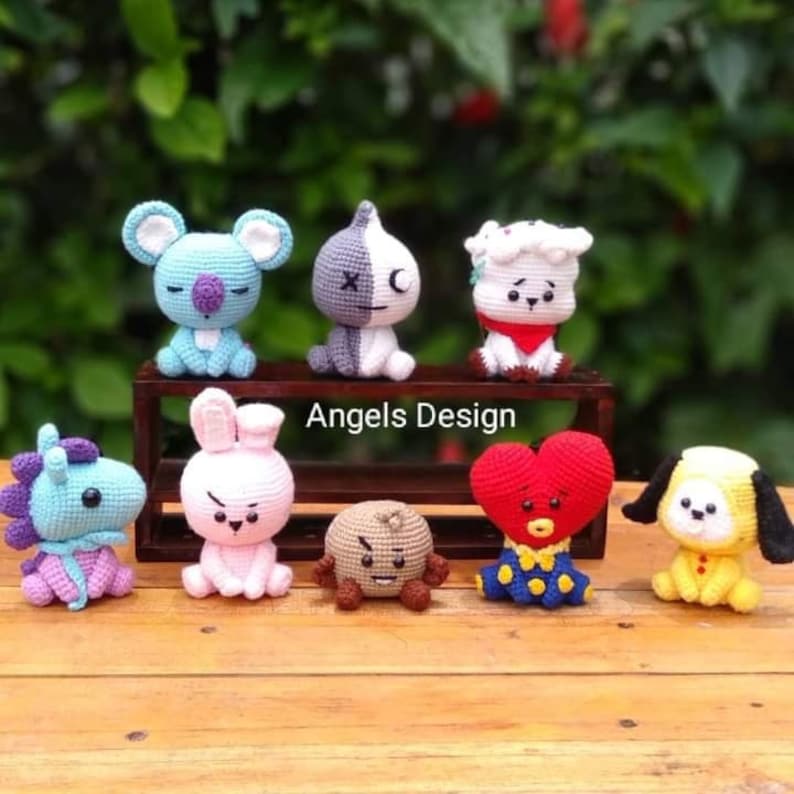 K&ouml;nnte beinhalten: Eine Sammlung von acht geh&auml;kelten Stofftieren, die jeweils einen anderen Charakter darstellen. Die Spielzeuge sind auf einem Holzregal angeordnet, auf dem der Text "Angels Design" aufgedruckt ist. Zu den Charakteren geh&ouml;ren ein blauer Koala, ein schwarz-wei&szlig;es Panda, ein wei&szlig;es Schaf, ein lila Einhorn, ein rosa Kaninchen, ein brauner B&auml;r, ein rotes Herz mit einem blauen Kleid und ein gelber Welpe.