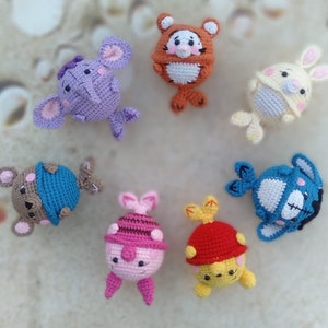 May include: A collection of seven crocheted stuffed toys, including a purple elephant, a brown tiger, a yellow bunny, a blue whale, a pink pig, a yellow chick, and a brown bear. The toys are all handmade and have embroidered faces.