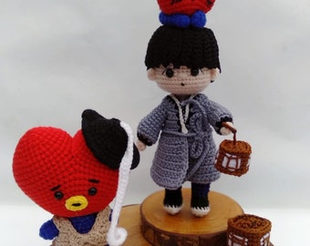 May include: Two crocheted plush toys, one a red heart-shaped character with a black hat and the other a gray-clothed character with a red heart on its head. Both are standing on wooden bases.