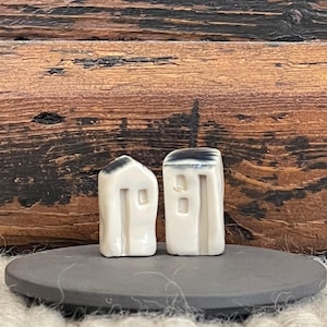 May include: Two small white ceramic houses with black accents, sitting on a gray stone base. The houses have simple rectangular shapes and small windows.