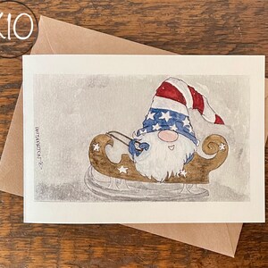 May include: A watercolor illustration of a gnome wearing a red, white, and blue hat with stars and riding a wooden sled with stars. The background is a light gray with a watercolor effect.