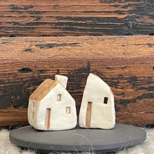 May include: Two small, hand-crafted ceramic houses with brown roofs and white walls. The houses are sitting on a black slate base.