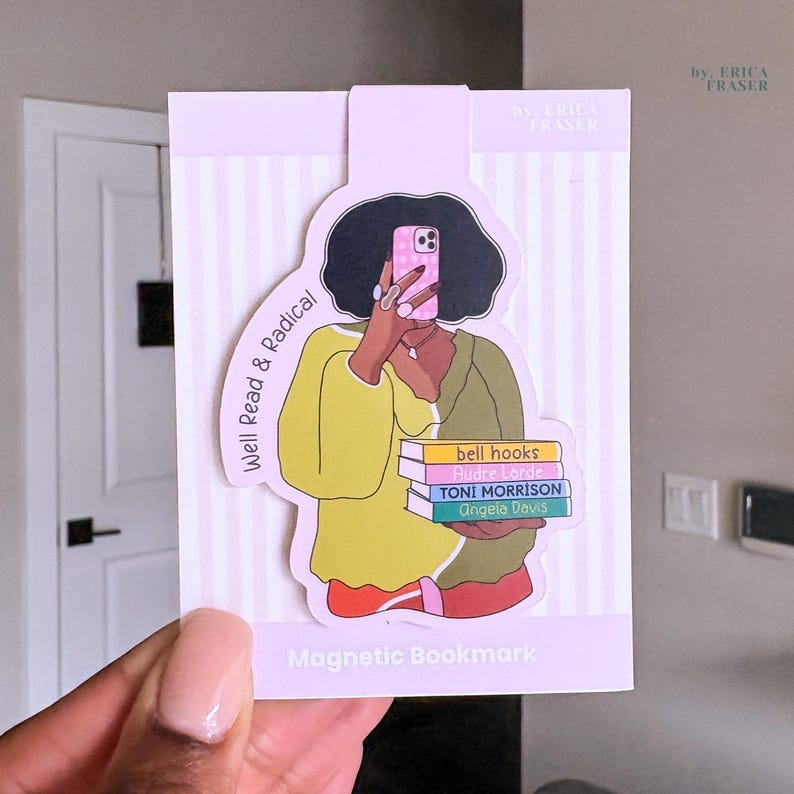 May include: A magnetic bookmark featuring an illustration of a person with dark hair holding a phone and a stack of four books. The books are labelled bell hooks, Audre Lorde, TONI MORRISON, and Angela Davis. The text Well Read & Radical is printed.