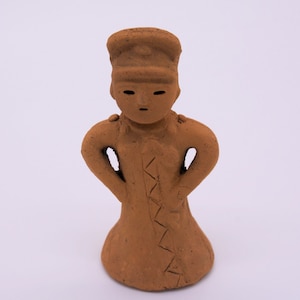 May include: A terracotta figurine of a person wearing a hat and a long robe. The figurine has a simple, stylised design and is made of a reddish-brown clay.