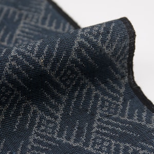 Może przedstawiać: Zbliżenie na ciemnoniebieski materiał z białym geometrycznym wzorem. Materiał ma fakturowaną powierzchnię i czarną obwódkę.