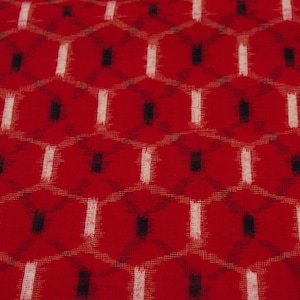 Pode incluir: Tecido vermelho com um padrão geométrico branco e preto. O padrão é um desenho repetitivo de pequenos quadrados e losangos.