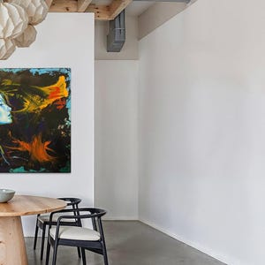 Pode incluir: Interior de uma sala de jantar moderna. Uma mesa redonda de madeira &eacute; combinada com cadeiras pretas com almofadas brancas. Uma pintura abstrata colorida est&aacute; pendurada na parede. Acima, h&aacute; lanternas de papel decorativas.
