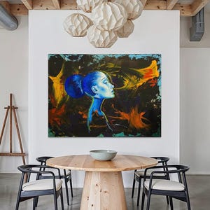 Pode incluir: Pintura abstrata do perfil de uma mulher em tons de azul, amarelo e laranja. A obra de arte est&aacute; pendurada acima de uma mesa de jantar redonda de madeira com cadeiras pretas. V&aacute;rias lumin&aacute;rias pendentes brancas em forma de globo iluminam a sala.