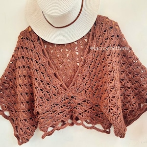 Op de afbeelding: Een bruin gecrochet top met een brede, open halslijn en wijde mouwen. De top is gemaakt met een delicate, kant-achtige steek en heeft een cropped lengte.