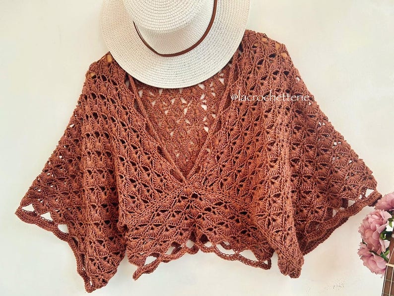 Op de afbeelding: Een bruin gecrochet top met een brede, open halslijn en wijde mouwen. De top is gemaakt met een delicate, kant-achtige steek en heeft een cropped lengte.